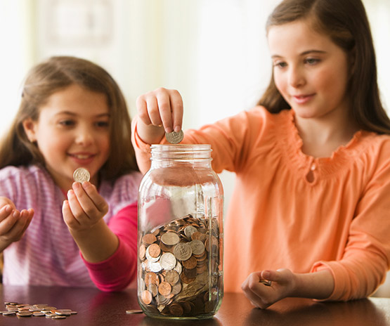 Two young girls putting money in jar
